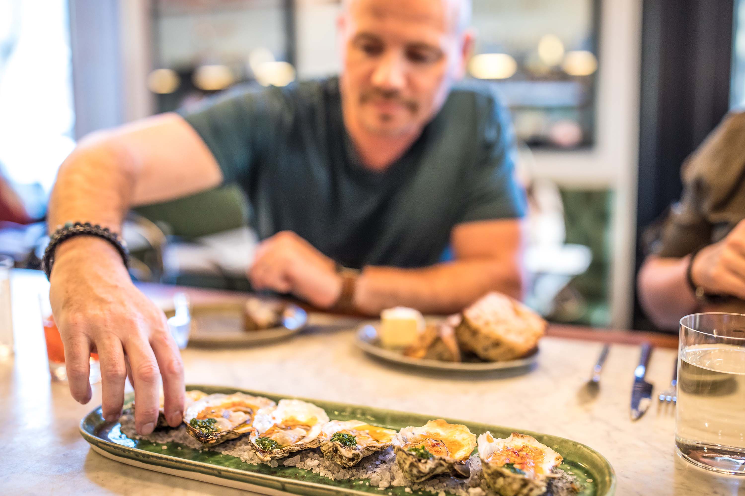 Downtown raleigh dt customer reaching for oyster from dish at bar resize